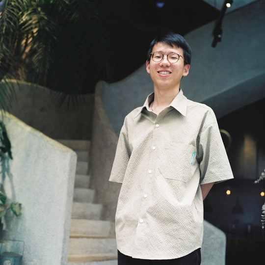 一个戴眼镜和白色衬衫的年轻男子站在一些楼梯前 手里拿着滑板。