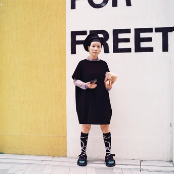 一位穿着黑色连衣裙的年轻女子站在一栋建筑物的墙上 前面有一个标志。