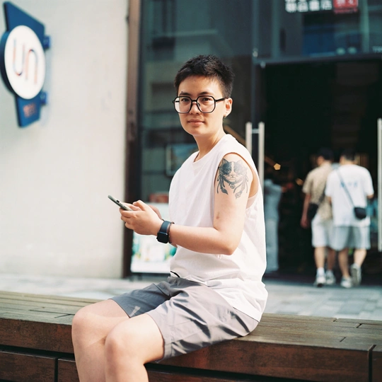 一个戴眼镜的年轻人坐在长凳上看手机