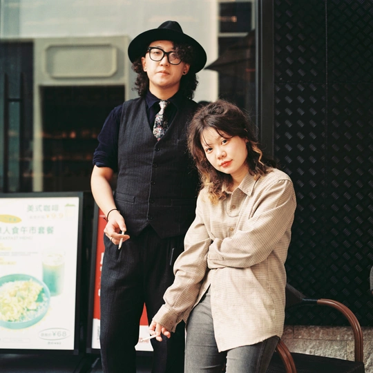 一顶帽子一个男人和一个小女孩站在人行道上 旁边有一把椅子。