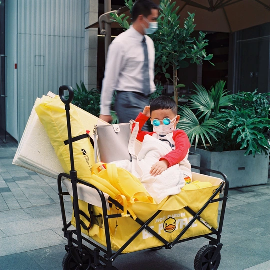 一个男子推着一个载有小孩的小车 而一个男子走在他身后。