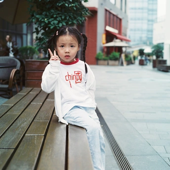 一个穿着白衬衫的小女孩坐在靠近桌子的一张木凳上