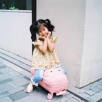 一个小女孩坐在人行道旁边的一个粉色箱子上 旁边有一栋建筑。