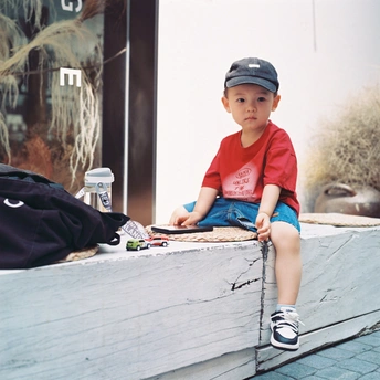 一个戴帽子和衬衫的小男孩坐在一个小长凳上