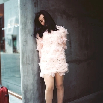 一位穿着短白色连衣裙的年轻女子 靠在红色行李箱旁边的一堵墙边。