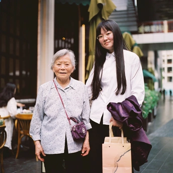一位老妇人走在一位年长妇女旁边 她手里有一个包。