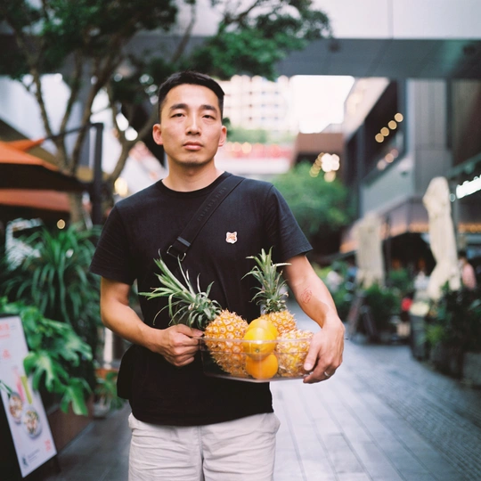 一位年轻人手里拿着一个菠萝和新鲜橙子