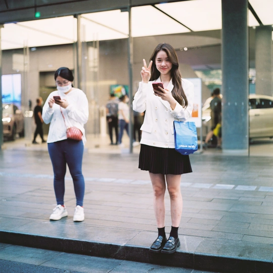 一位年轻女子站在另一位年轻女子旁边 手里拿着手机。
