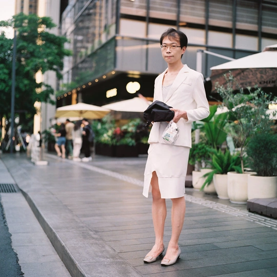 一位穿着白色连衣裙的女人走在人行道上 手里拿着一个包和一把伞。