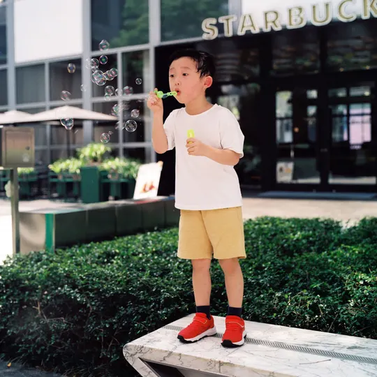 一个小男孩站在一个小凳子上吹泡泡。