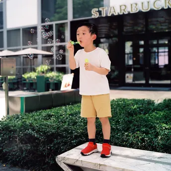 一个小男孩站在一个小凳子上吹泡泡。