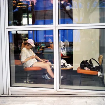 一个年轻女子坐在商店窗户前的一个长椅上 一只猫坐在橙色椅子上。