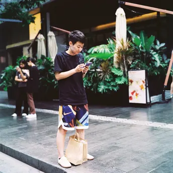 一名年轻男子站在人行道上 一边拿着手机 一边看着手机。