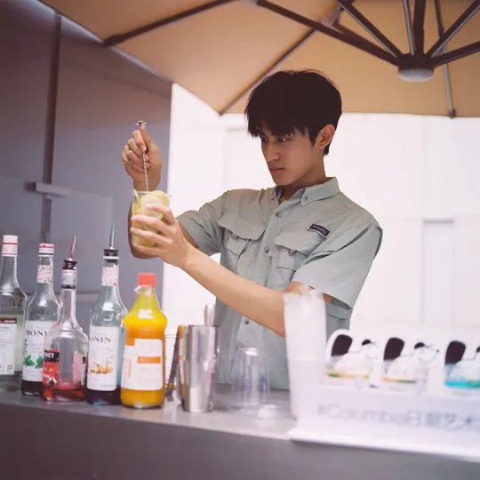 一个年轻男子站在柜台后面 从瓶子里倒饮料到玻璃杯中。