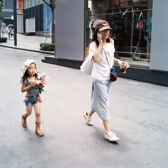 一个妇女正在打电话 带着一个小女孩在街上走 小女孩在人行道上走。