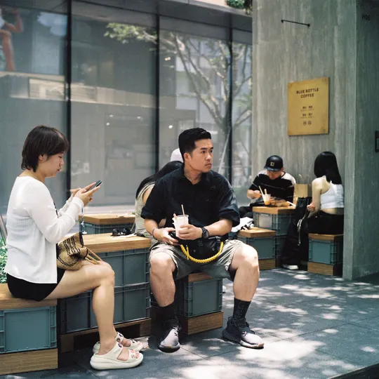 一个男人和一个女人坐在建筑物前的一张长椅上 同时看着他们的手机。