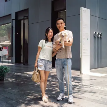 一名年轻男子和女子抱着一只小狗站在人行道上 前方是一座建筑。