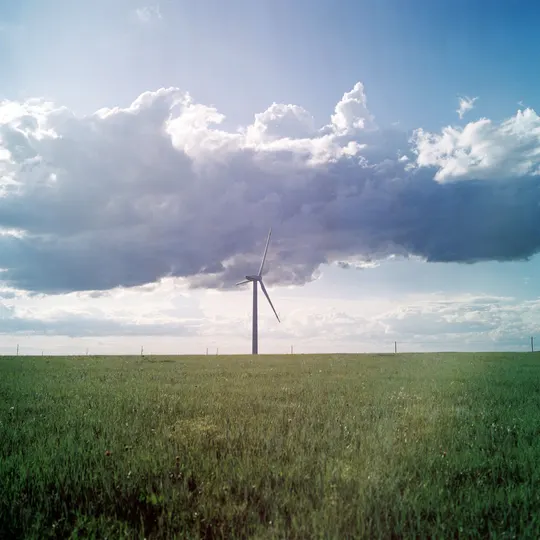 一片绿色的田野上有一座风车 天空中有一朵蓝色的云和一朵白云。