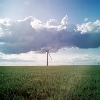 一片绿色的田野上有一座风车 天空中有一朵蓝色的云和一朵白云。