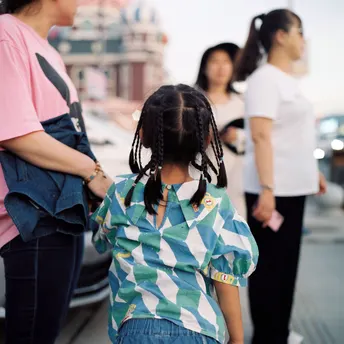 一个年轻女孩和她妈妈正在街上走 其他人在人行道上站着。