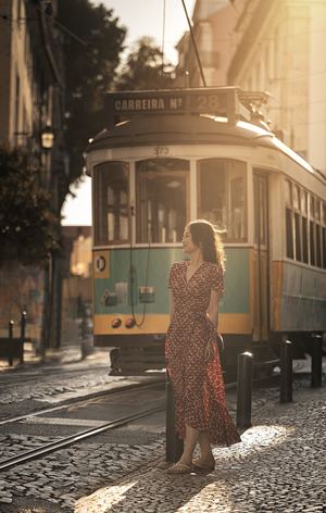 一个穿着连衣裙的女人走在一条靠近有轨电车的老街上