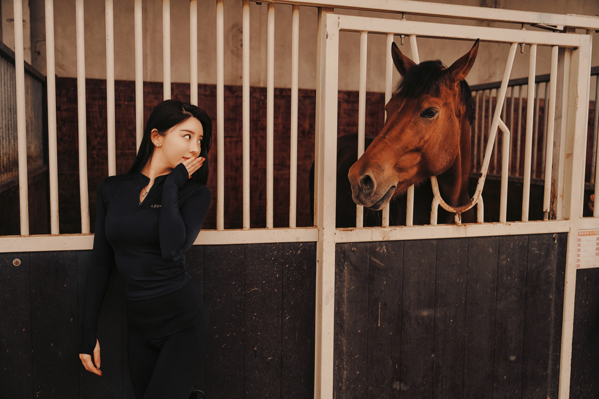 一个女人站在谷仓的马厩里看着一匹棕色的马
