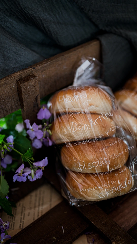 一个装满甜甜圈的盒子放在一张木桌上 旁边是一个装满鲜花的塑料袋