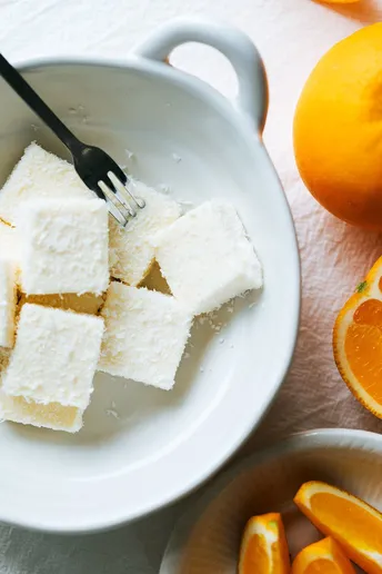 一个带有蛋糕方块和叉子的白盘子 旁边放着一个装满糖和橙子的碗。