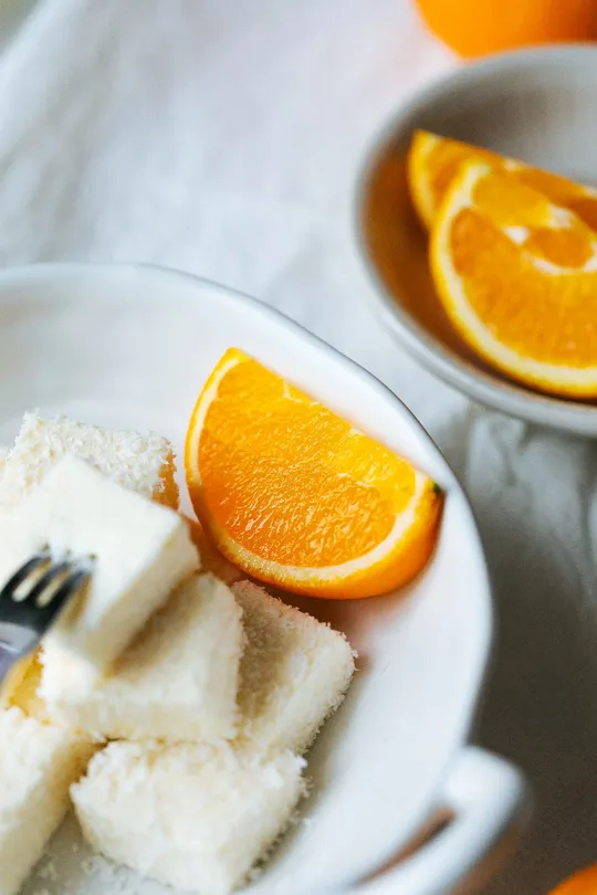 一块白盘子 一个叉子 一个装有粉末糖的碗 一个橙片 放在桌子上的一块白盘子上。