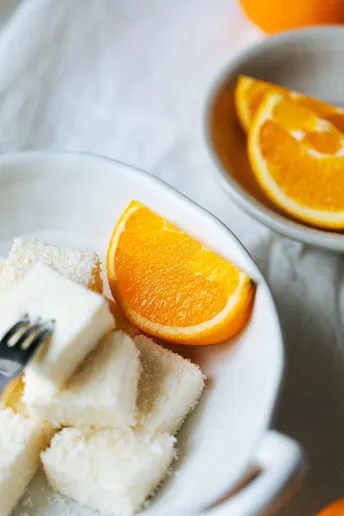 一块白盘子 一个叉子 一个装有粉末糖的碗 一个橙片 放在桌子上的一块白盘子上。