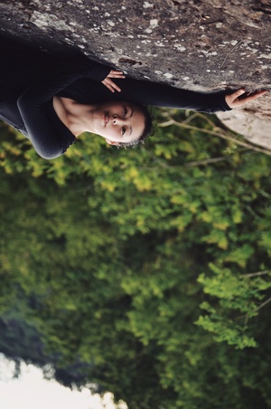 一位年轻女子正在攀爬一块巨大的岩石 上方挂着树木。