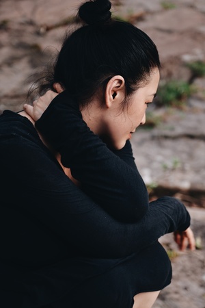 一个穿黑色衣服的年轻女子坐在岩石上 双手紧握在一起。