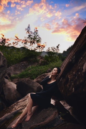 一个年轻女子坐在夕阳下的大型岩石上