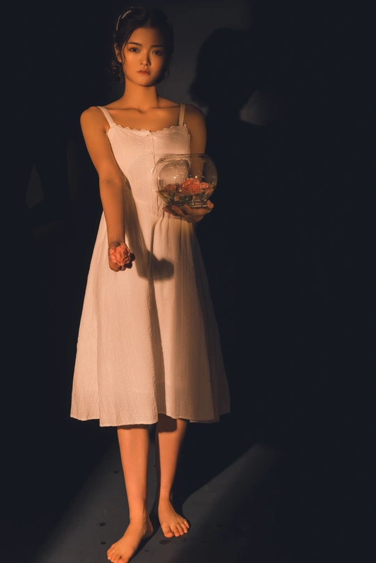 在昏暗的光线下 一位身穿白色连衣裙的年轻女子手里拿着一罐玫瑰