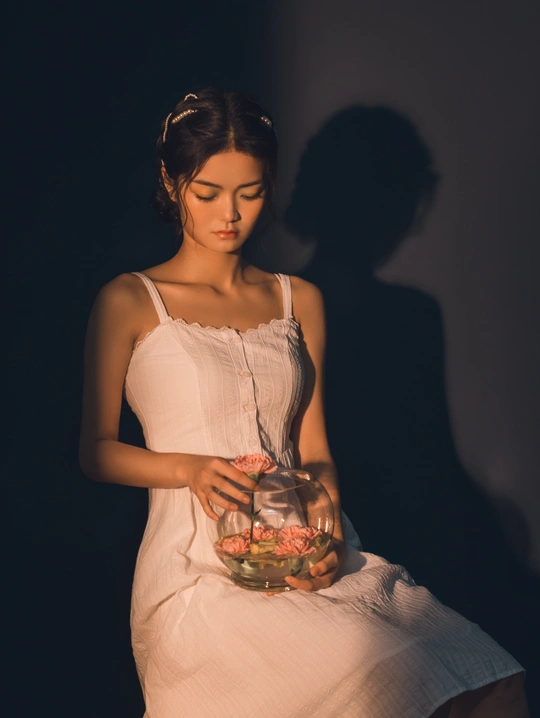 一个穿着白色连衣裙的孕妇手里拿着一碗花和一条金鱼