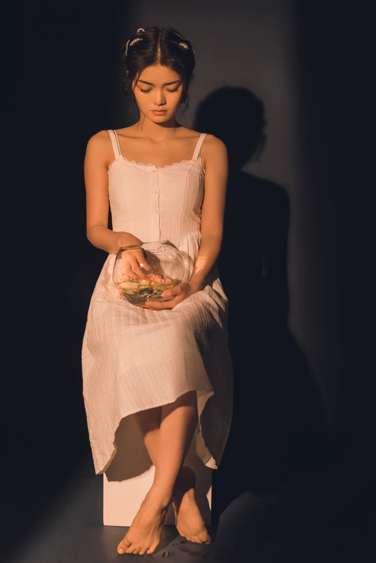 一位身穿白色连衣裙的年轻女子站在黑色背景上 手里拿着食物