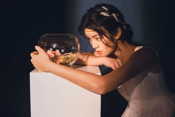 一个年轻的女人手里拿着一碗花 看着白色底座上鱼缸里的鱼