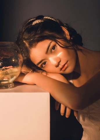 一位年轻女子拿着一条金鱼坐在白色桌子上水族馆旁边的碗里