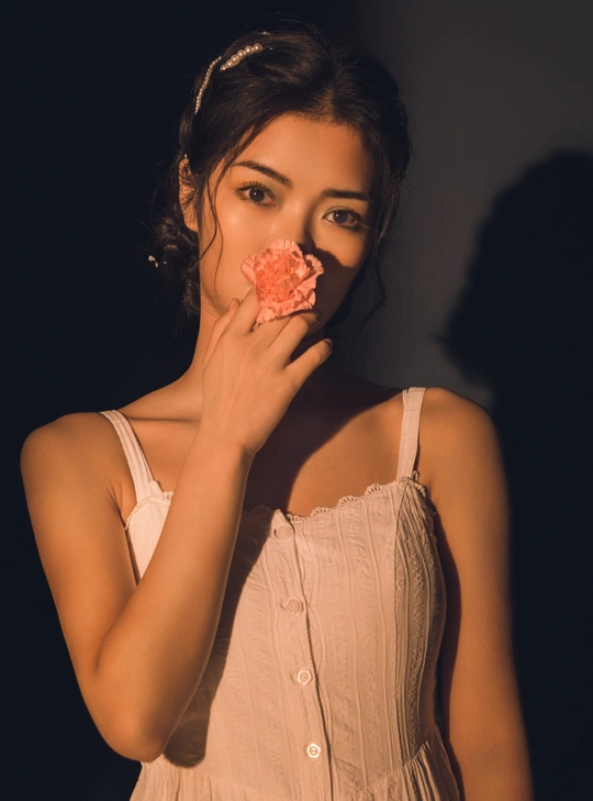 一个穿着白色连衣裙的年轻女子手里拿着一朵粉红色的花