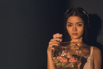 一位手里拿着一碗玫瑰的年轻女子在黑色背景前摆姿势