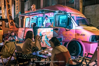 人们坐在一辆粉红色面包车前的桌子旁