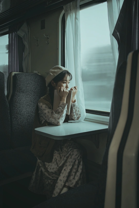 一个年轻女子坐在火车上 正在透过窗户看外面 手里拿着一杯茶。