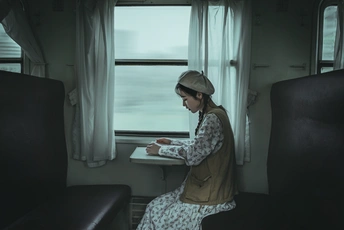 一个年轻女子坐在火车上的一把椅子上 正在看着桌子上的笔记本电脑。