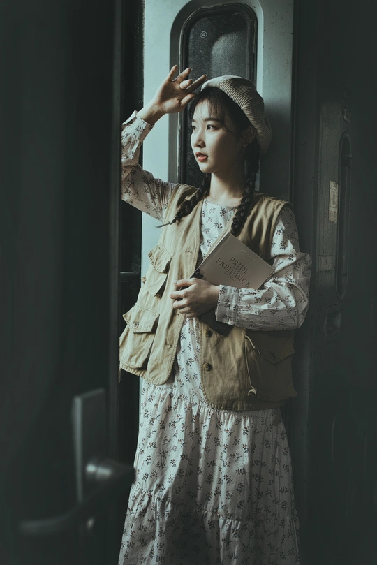 一位穿着连衣裙和帽子的小姐拿着一本书 并凝视着火车窗户。