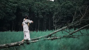 一位穿着白色连衣裙的女人穿过一片绿色的草地上树木。