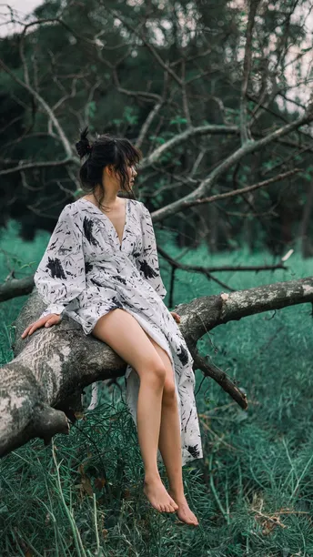一位穿着连衣裙的年轻女子坐在树林中的一棵树的树枝上