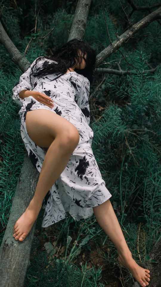 一位穿着连衣裙的女人在森林里爬上一棵树