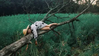 一位年轻女子躺在一片绿色草地上 靠近一棵倒下的树。