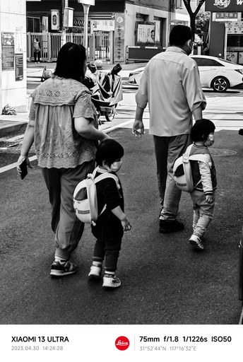 一张黑白照片 一位女子抱着一个年轻男孩 男孩手牵着其他人和成年人 沿着繁忙的街道走。