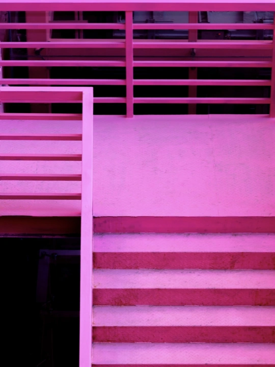 一个玩滑板的女人坐在粉红色的墙、红色的长椅和楼梯前